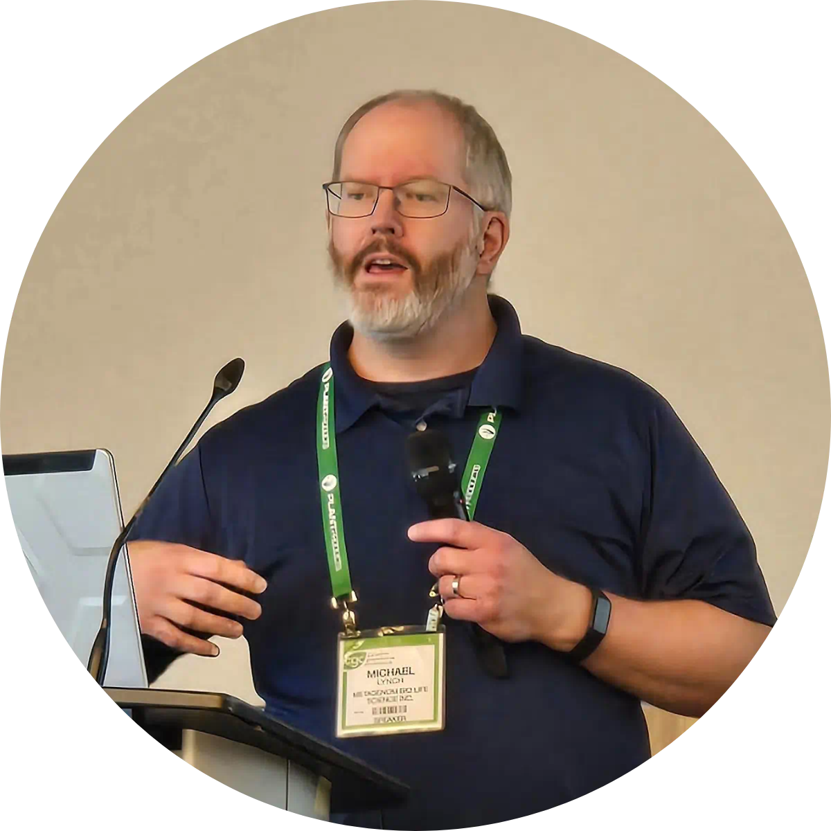 Profile photo of Dr. Michael D.J. Lynch speaking at a greenhouse and agriculture conference, holding a microphone and wearing a conference badge.